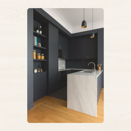 Cuisine moderne avec façades noires mates et îlot central en marbre blanc, plan de travail élégant et suspensions noires minimalistes au plafond.