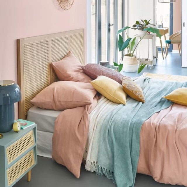 Chambre bohème avec tête de lit en rotin naturel, coussins colorés et ambiance chaleureuse.